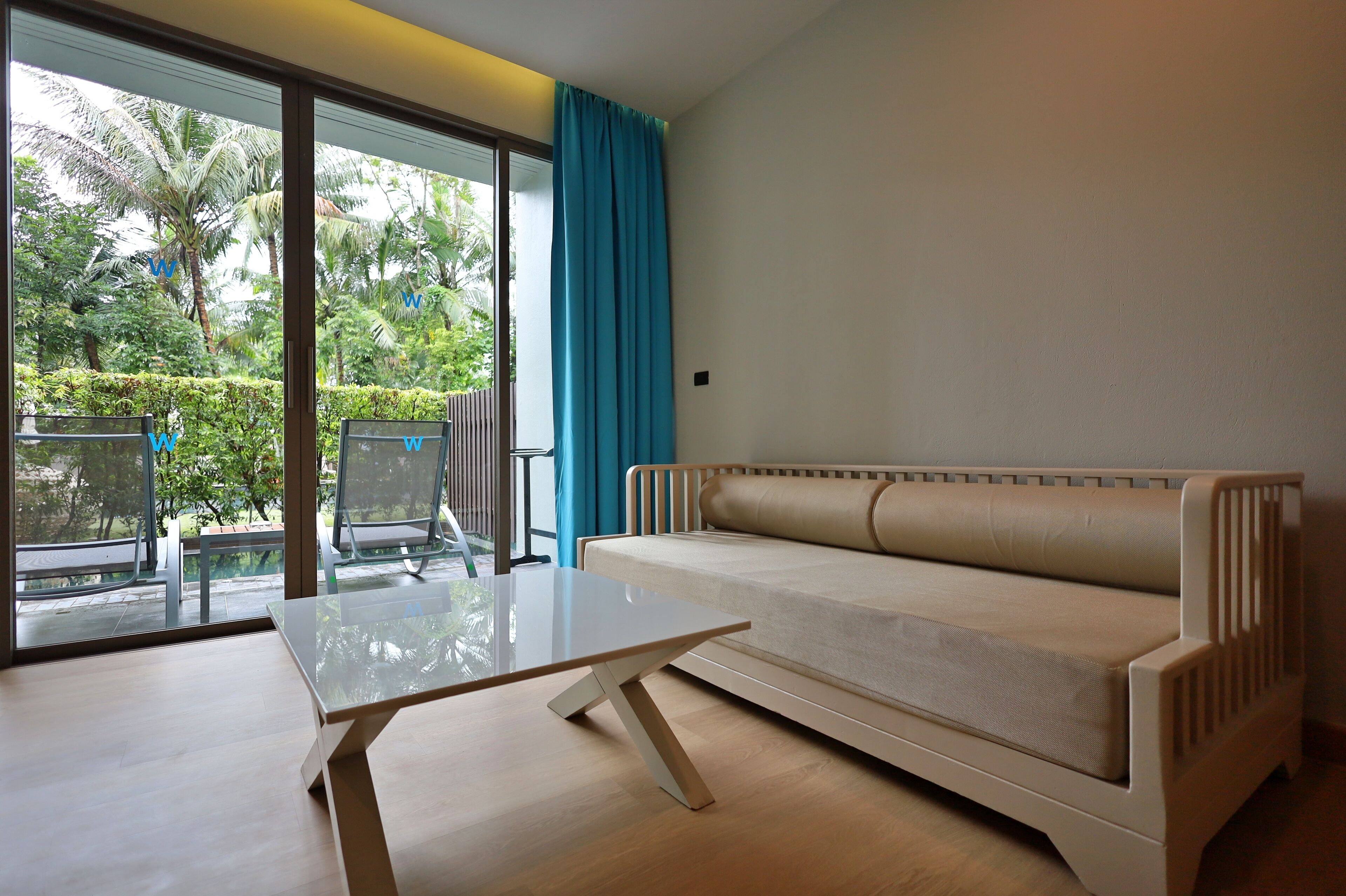 A modern room with a glass table, beige sofa, and a view of greenery through large windows.