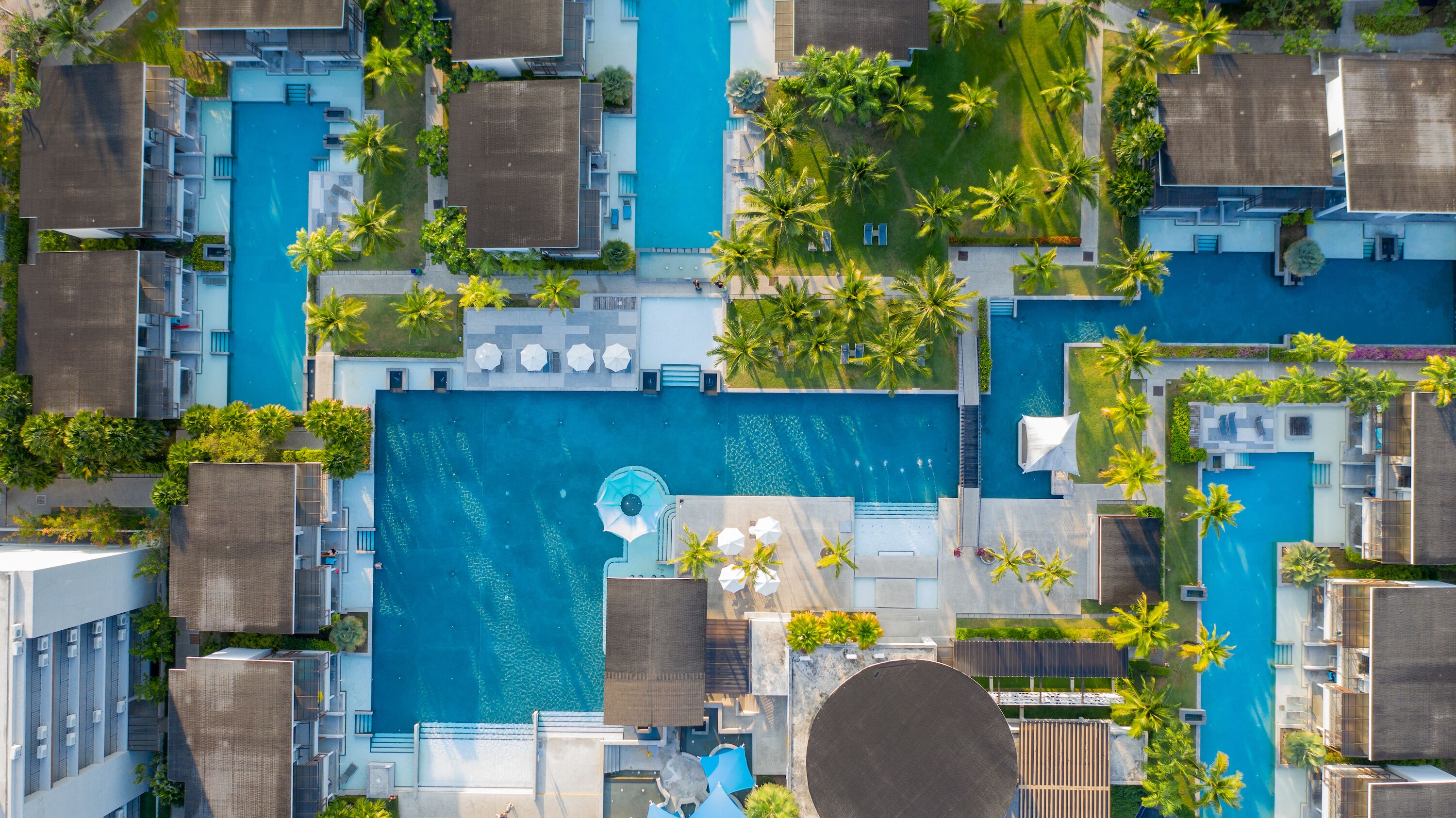 Vue aérienne d’un complexe hôtelier doté de plusieurs piscines, de palmiers et de bâtiments modernes.
