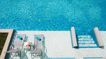 A clear blue pool with lounge chairs and a table, surrounded by a tiled deck.