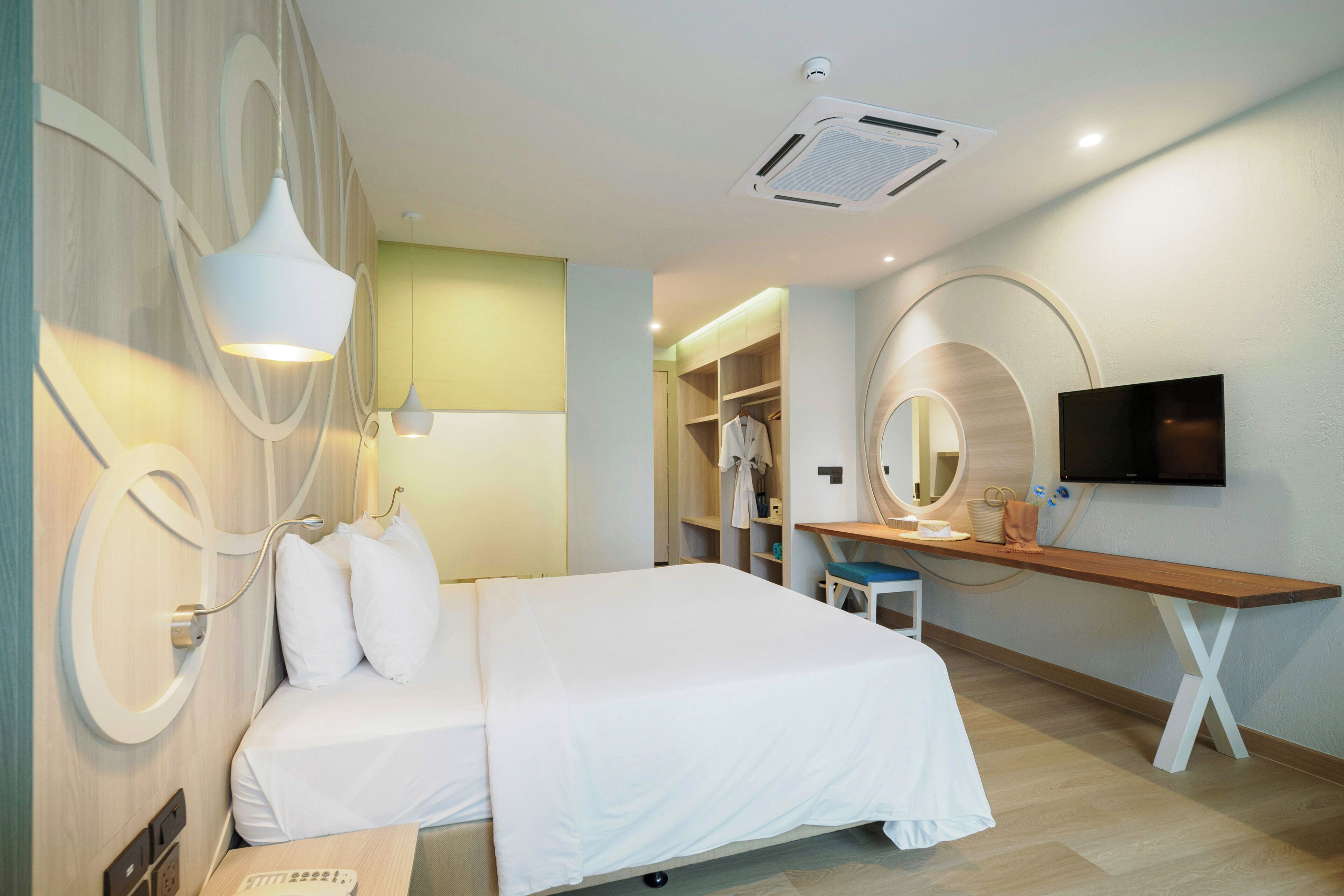 A modern hotel room with a bed, bedside lamps, a desk, a TV, and a wardrobe.