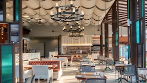 Un vaste espace de restauration intérieur doté de hauts plafonds, de lustres modernes et de différents types de sièges, notamment des tables et des banquettes.
