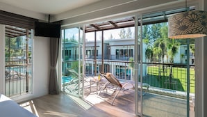 Une chambre d’hôtel moderne dotée de grandes fenêtres, d’un balcon avec vue sur la piscine et d’un téléviseur à écran plat fixé au mur.