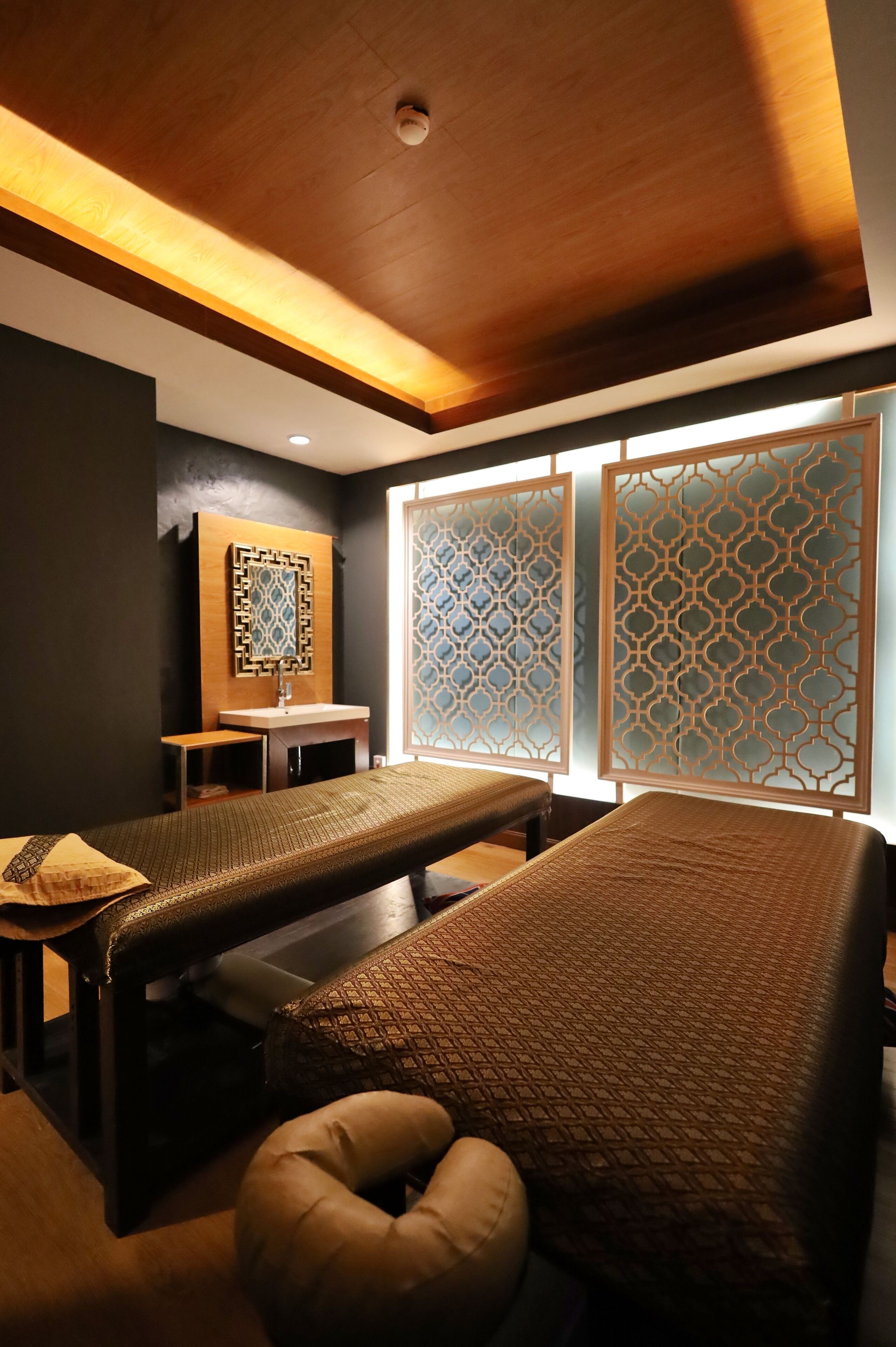 Een kamer met twee massagetafels, een klein tafeltje met een wastafel en decoratieve schermen.