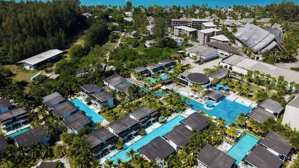 Vue aérienne d’un complexe hôtelier doté de plusieurs piscines, de villas en bord de mer et d’une végétation luxuriante.