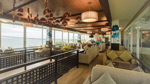 A spacious lounge area with multiple seating options, large windows offering a view of the sea, and decorative hanging lamps. - Seaside Resort (Ho Chi Minh City)