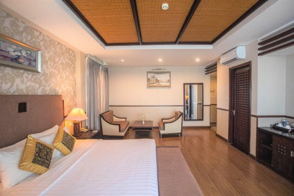 A hotel room with a large bed, two armchairs, a small table, and a desk.
