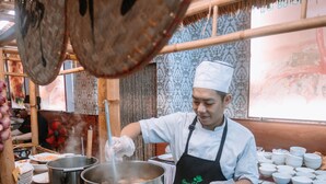 A chef preparing food in a traditional kitchen with bamboo structures and a thatched roof. - Seaside Resort (Ho Chi Minh City)