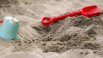 A beach scene with a blue bucket and a red shovel on the sand.