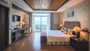 A hotel room with a bed, bedside tables, a desk, a TV, and a balcony with a view. - Seaside Resort (Ho Chi Minh City)