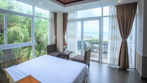 A hotel room with a large bed, a small table, a chair, and a balcony with a view of the sea. - Seaside Resort (Ho Chi Minh City)