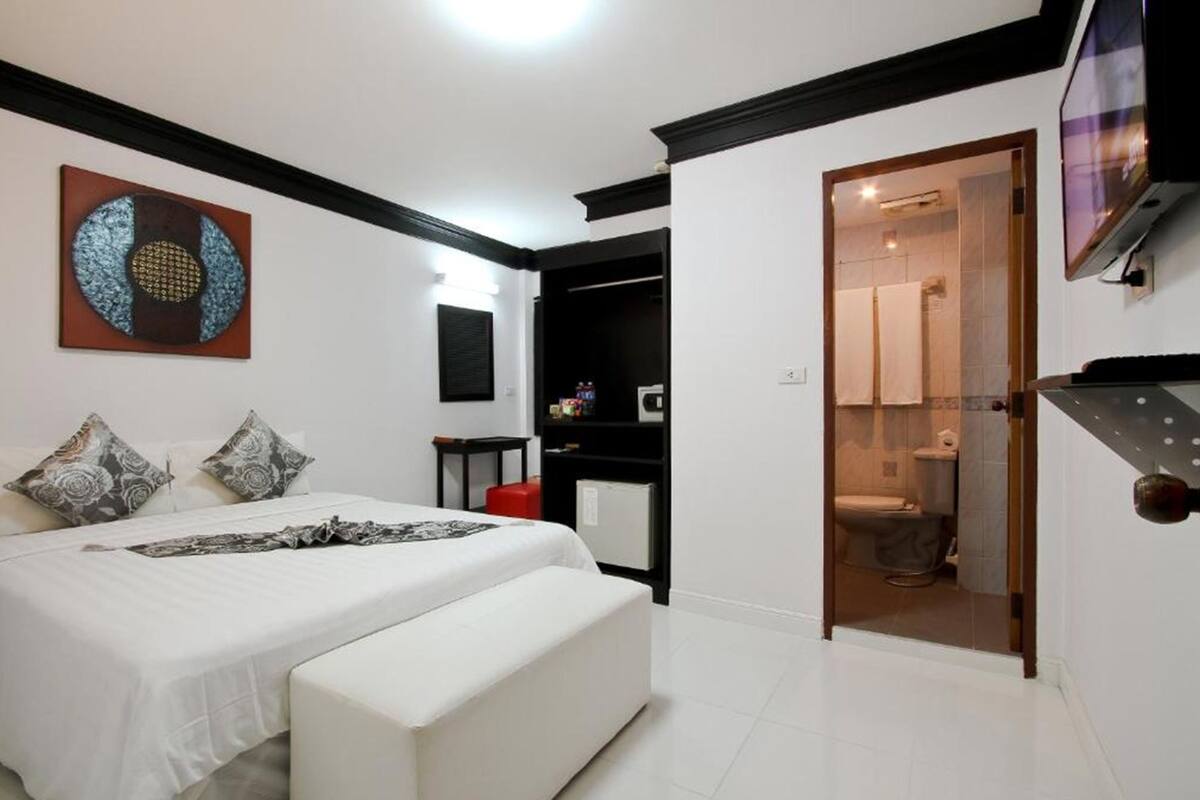 A modern bedroom with a bed, bedside tables, a TV, and a bathroom visible through an open door.