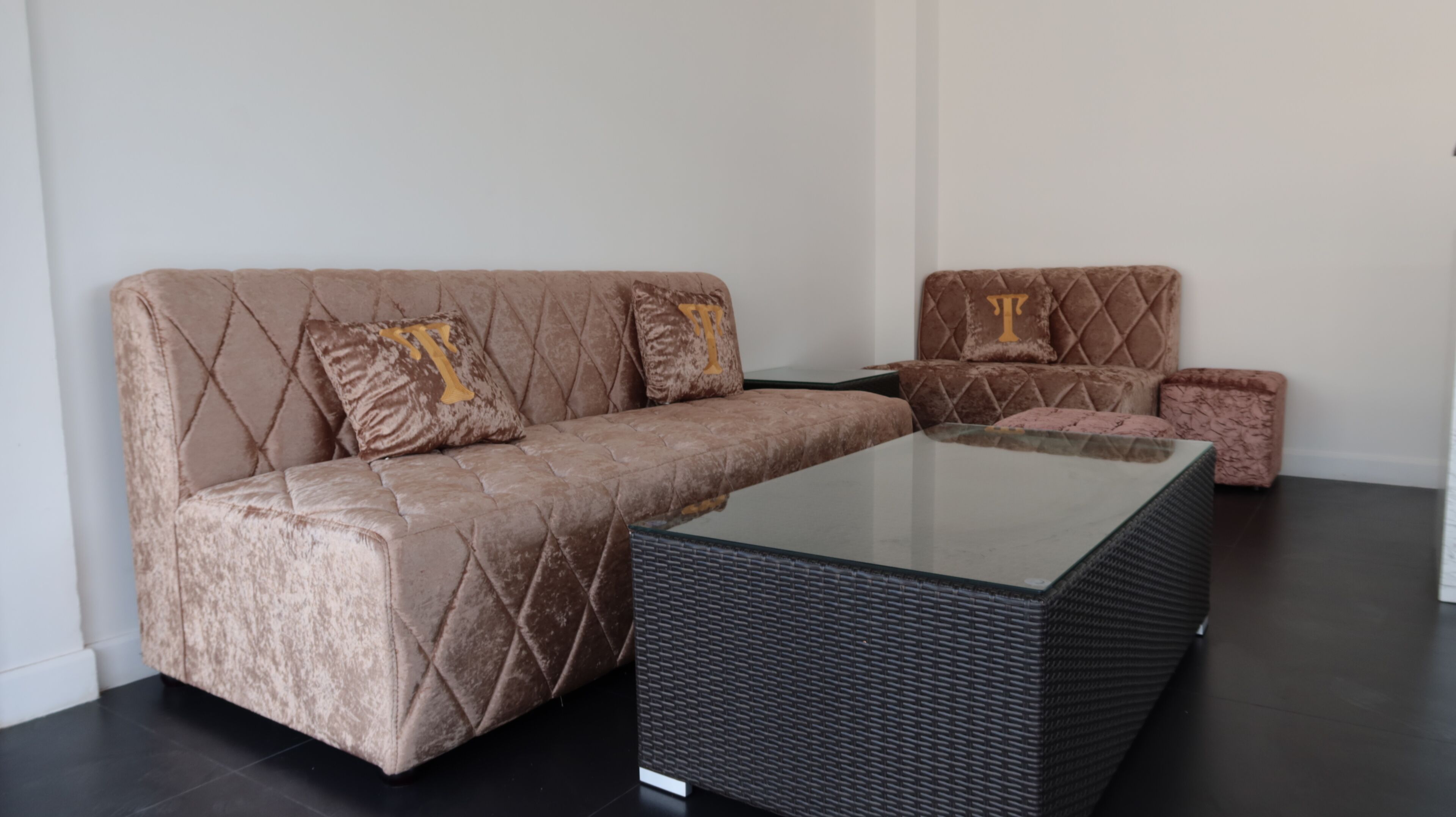 A modern living room with a brown velvet sofa, two matching armchairs, and a glass coffee table.