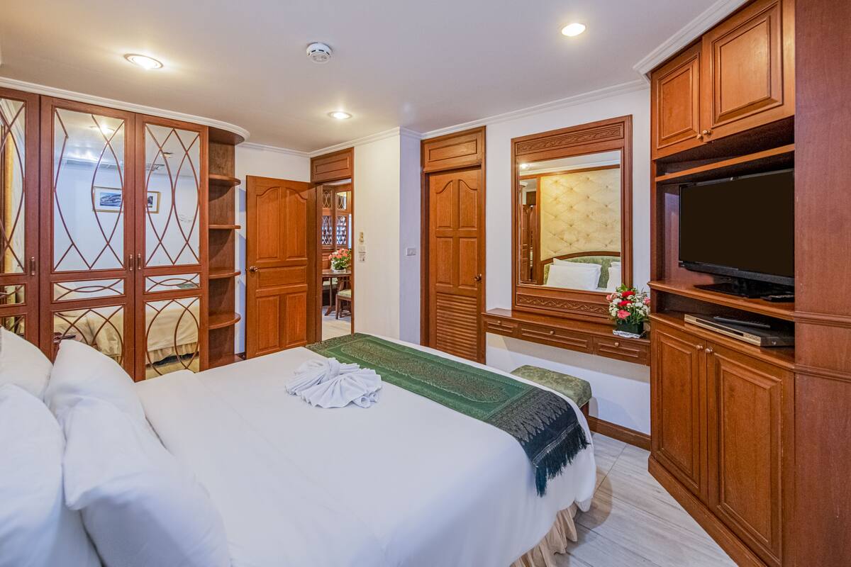 A hotel room with a large bed, wooden wardrobe, a television, and a mirror.