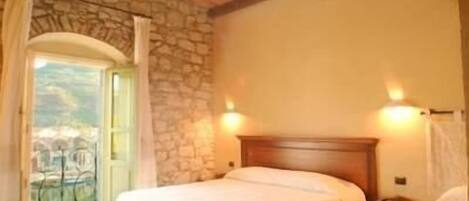 A bedroom with two beds, a stone wall, and a balcony with a view.
