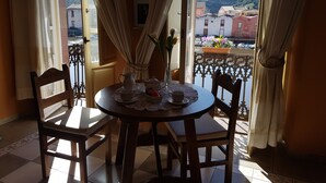Een eethoek met een tafel gedekt voor twee personen, een vaas met bloemen en uitzicht op een stad door een raam.