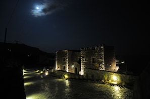 A stone building with a tower, illuminated by street lights, under a night sky with a visible moon.