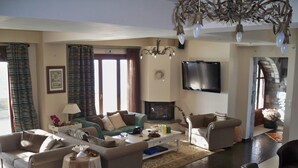A spacious living room with a fireplace, comfortable seating, a flat-screen TV, and a chandelier.