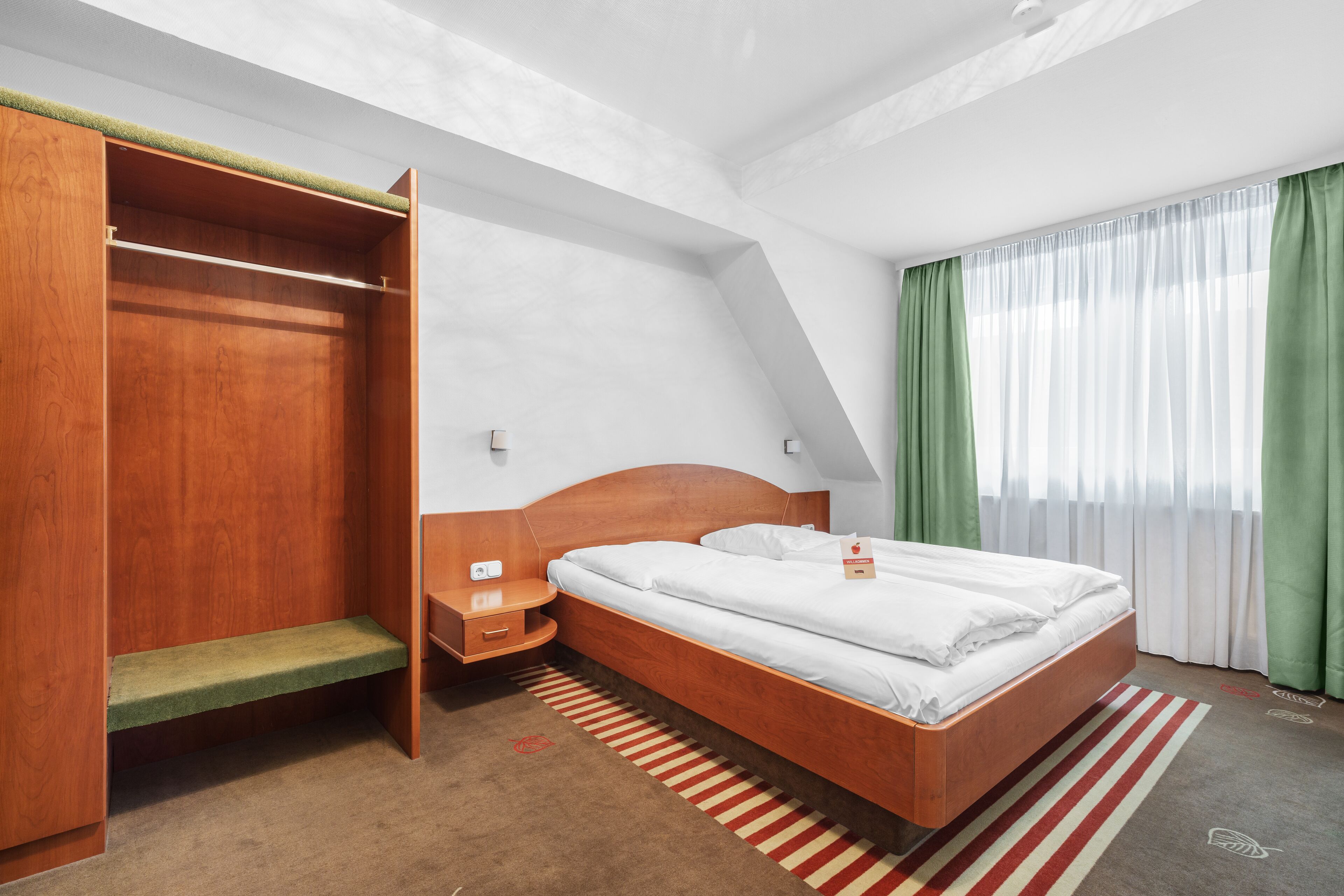 Ein Hotelzimmer mit einem hölzernen Bett, einer Bank, einem Nachttisch und einem Kleiderschrank.