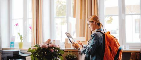 A person at a reception desk with a laptop, a plant, and a vase of flowers.
