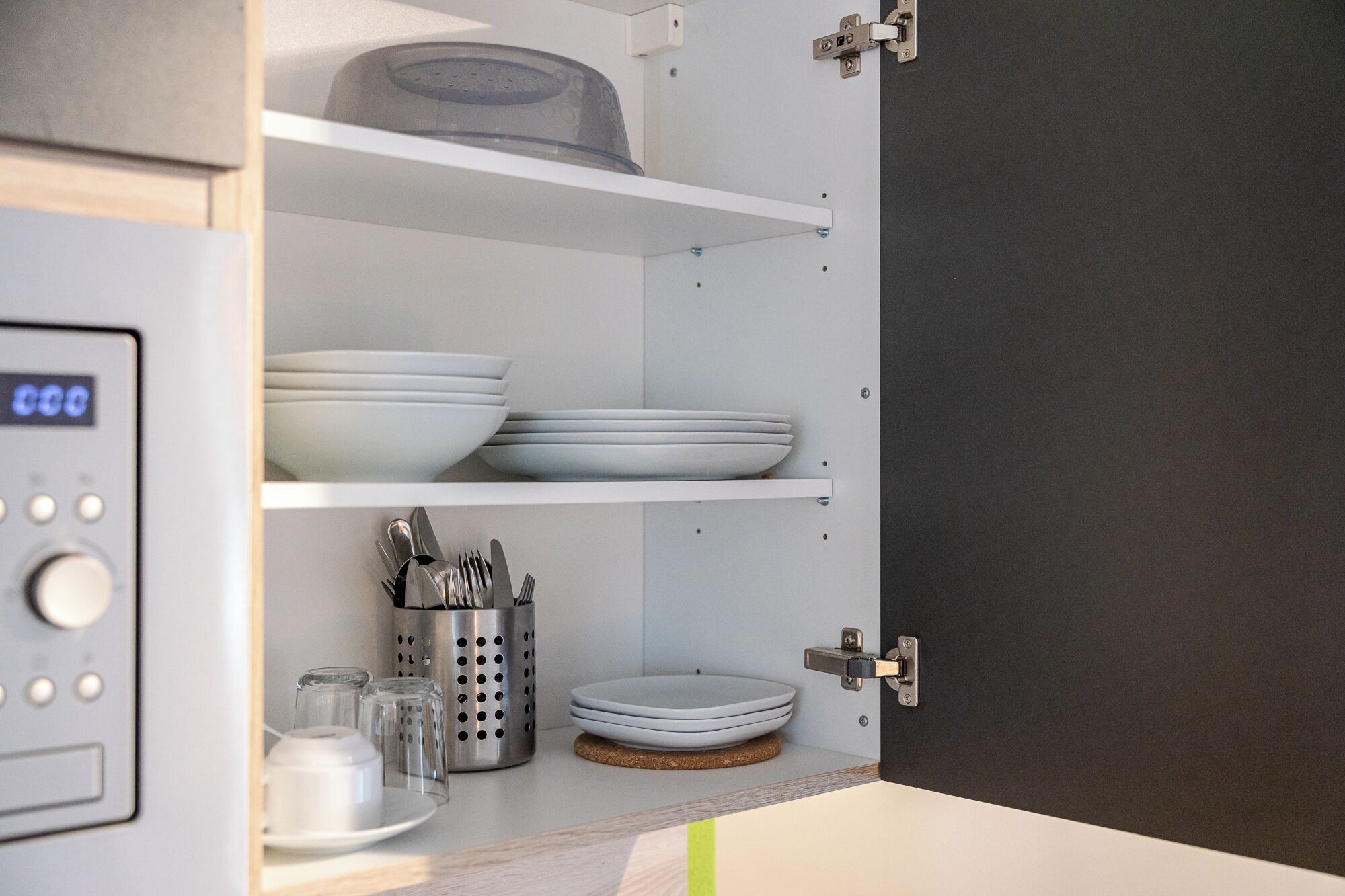 Una cocina con estantes blancos, una cafetera y un posavasos de corcho.
