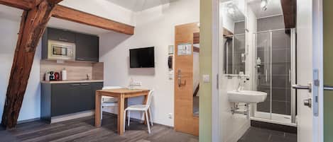 A modern kitchen with a microwave, a dining table with chairs, a TV, and wooden beams.