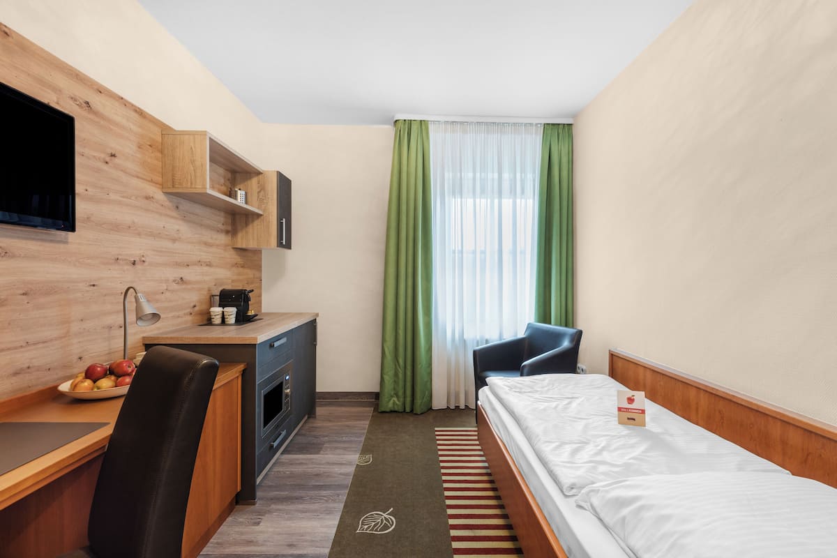A hotel room with a wooden desk, a bed, a chair, a TV, and a window with green curtains.