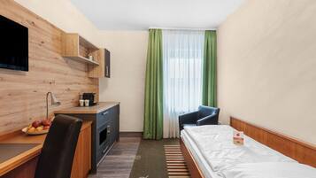 Une chambre d’hôtel avec un bureau en bois, un lit, une chaise, une télévision et une fenêtre avec des rideaux verts.