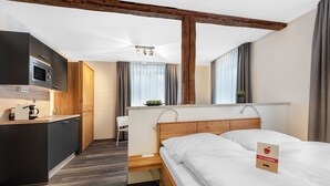 Una habitación de hotel moderna con techo de madera, una cama, un escritorio, una kitchenette y vistas al exterior.