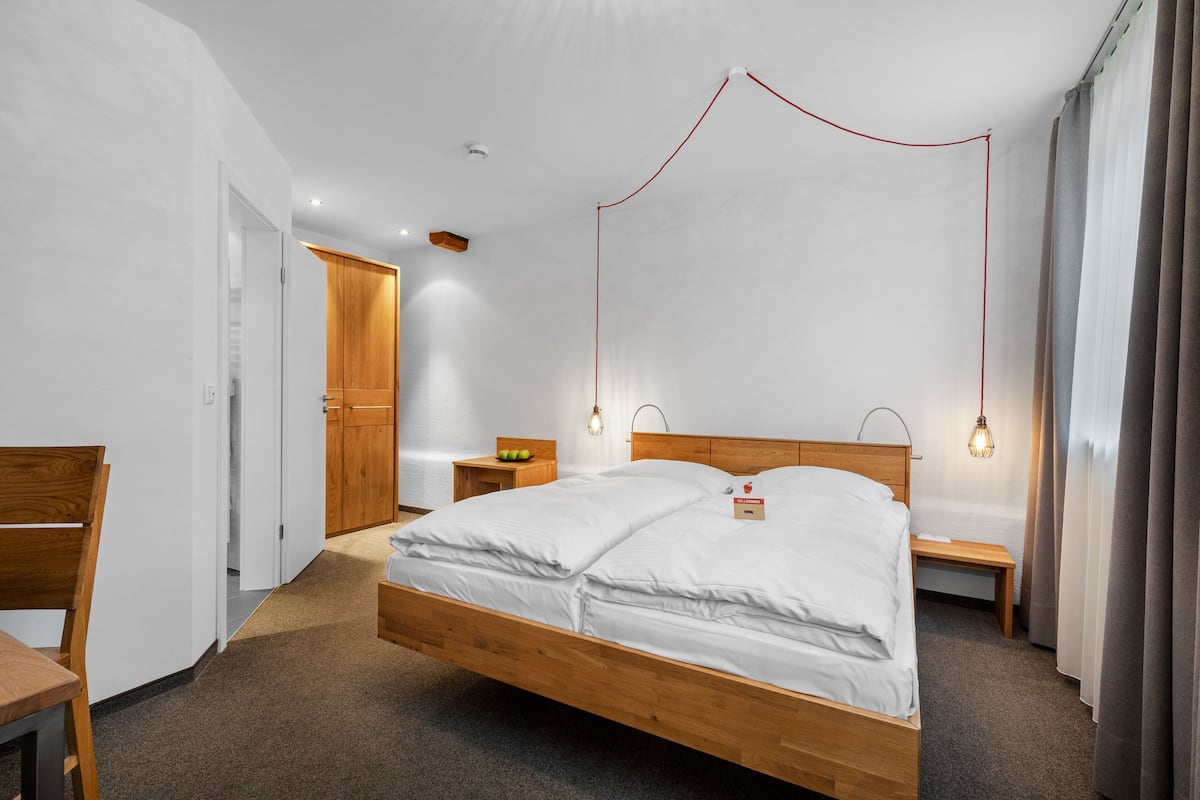 A modern hotel room with a wooden bed, bedside tables, a desk, and a wardrobe.