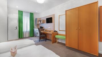 Ein Hotelzimmer mit zwei Betten, einem Schreibtisch, einem Stuhl, einem Kleiderschrank und einem Fernseher.