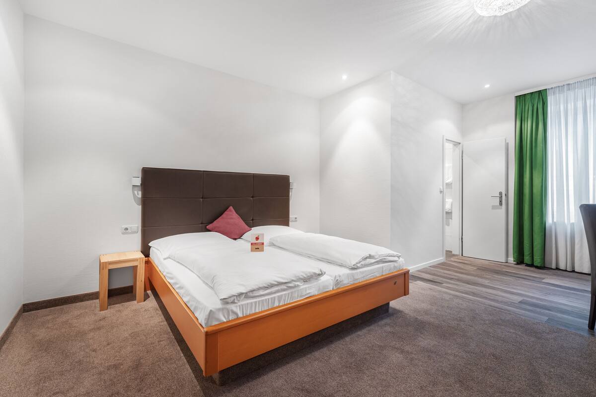 A modern hotel room with a wooden bed, a small bedside table, and a green curtain.