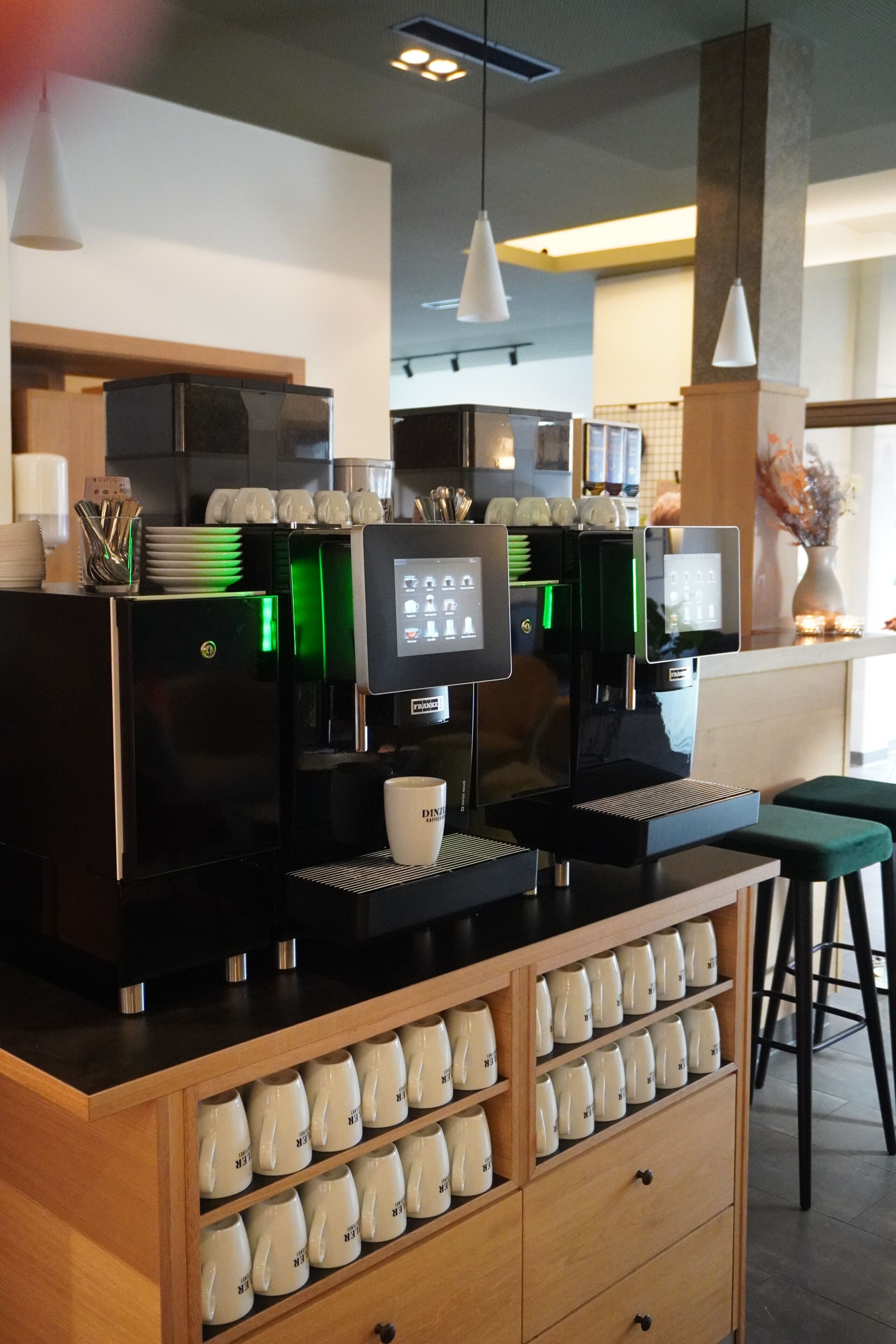 A coffee shop with two espresso machines, a digital display, and a counter with cups and a cash register.