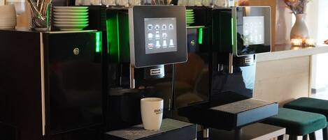 A coffee shop with two espresso machines, a digital display, and a counter with cups and a cash register.