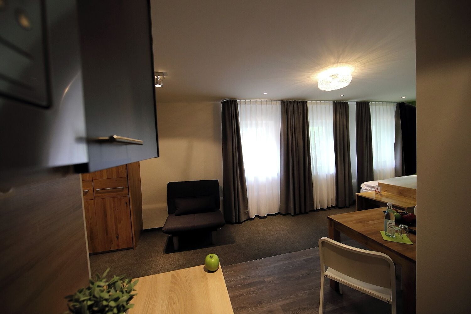 A compact hotel room with a kitchenette, a dining area, and a bed.