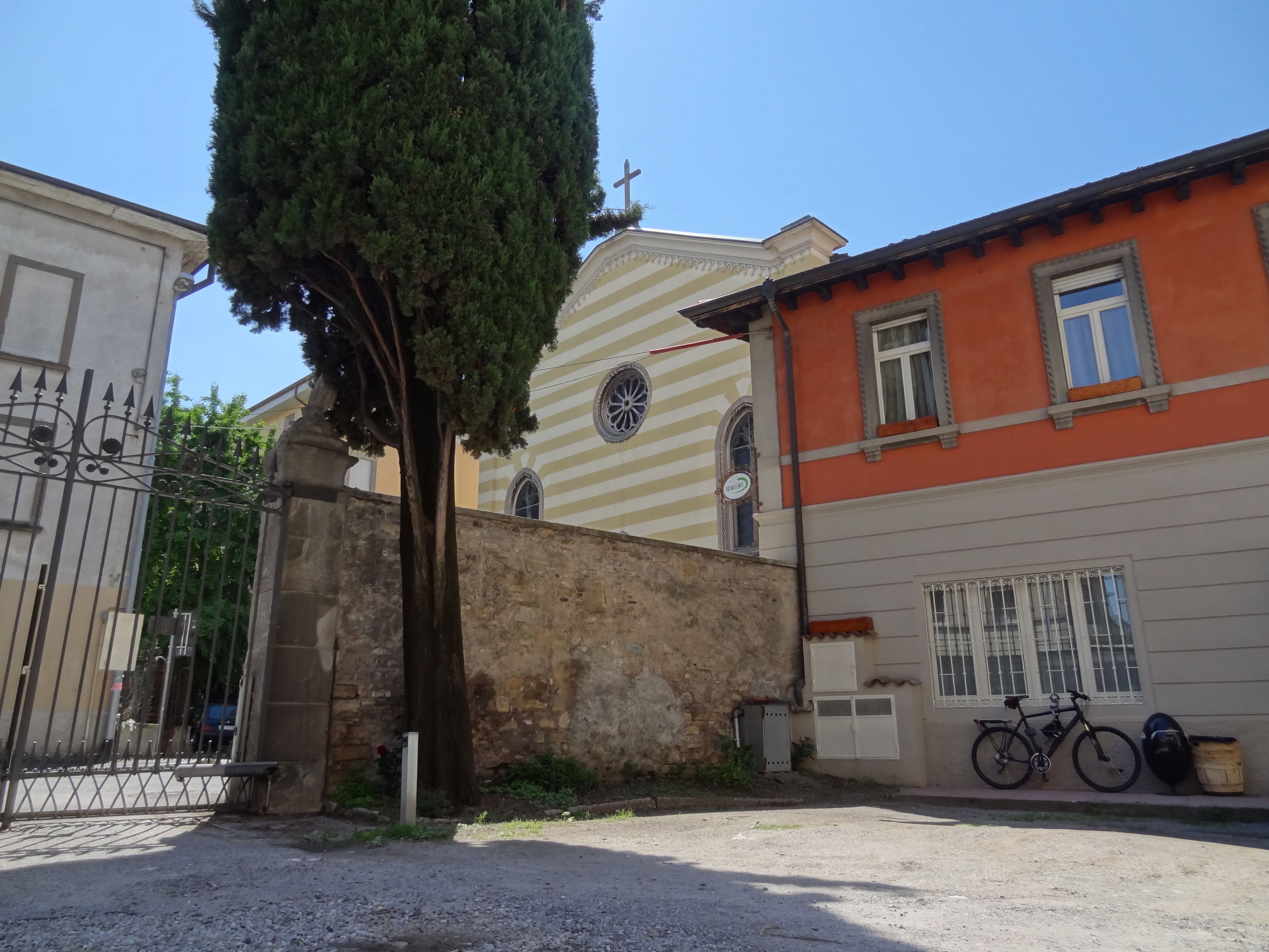 A street view with a gated entrance, a tree, and buildings with distinct architectural styles.