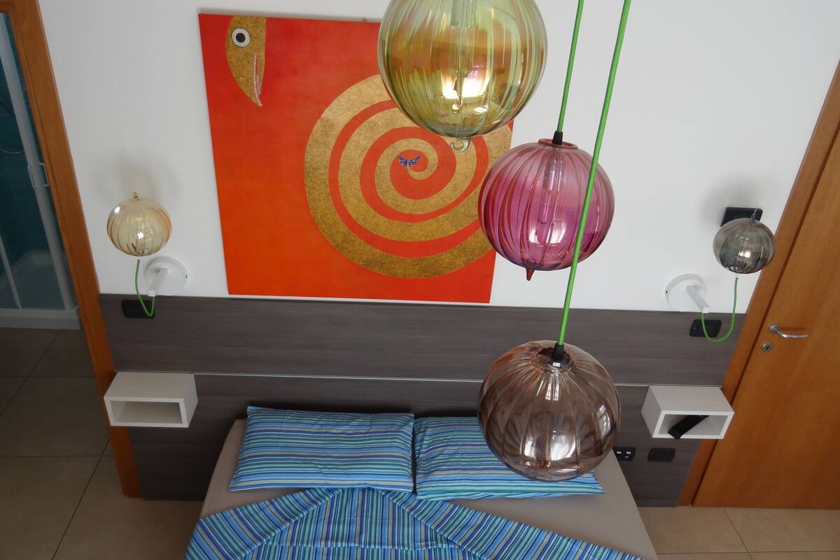 Un dormitorio con una cama, una obra de arte en la pared y tres lámparas colgantes.