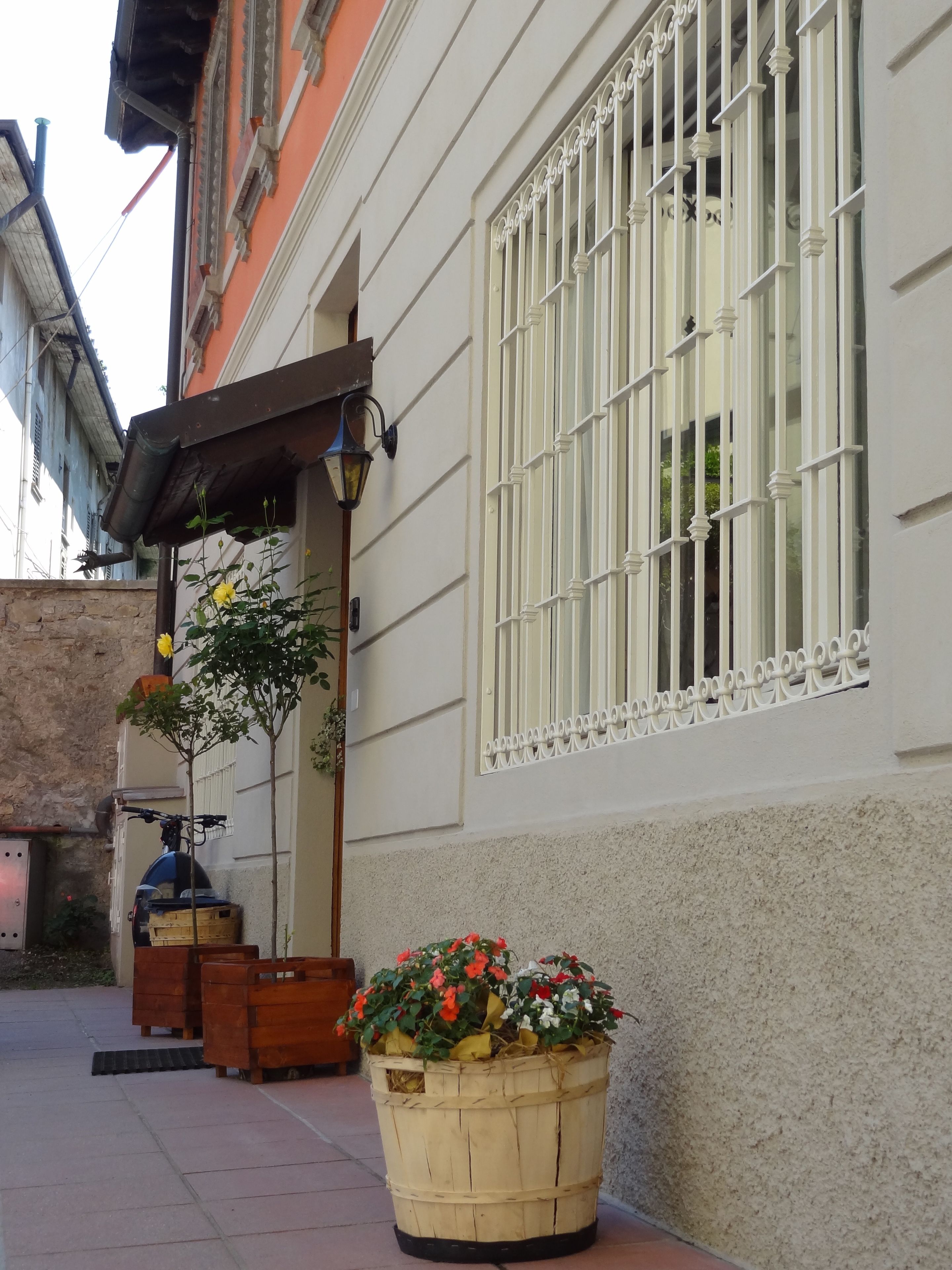 Ein Gebäude mit weißer Fassade, einem Fenster mit weißen Gitterstäben, einem kleinen Balkon und einem Holz-Blumenkasten.