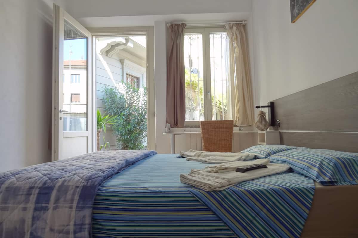 Un dormitorio con cama, una silla, una ventana y un radiador.