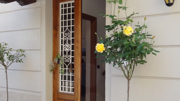Una puerta de madera con una celosía decorativa, un rosal amarillo en maceta y un farol en la pared.
