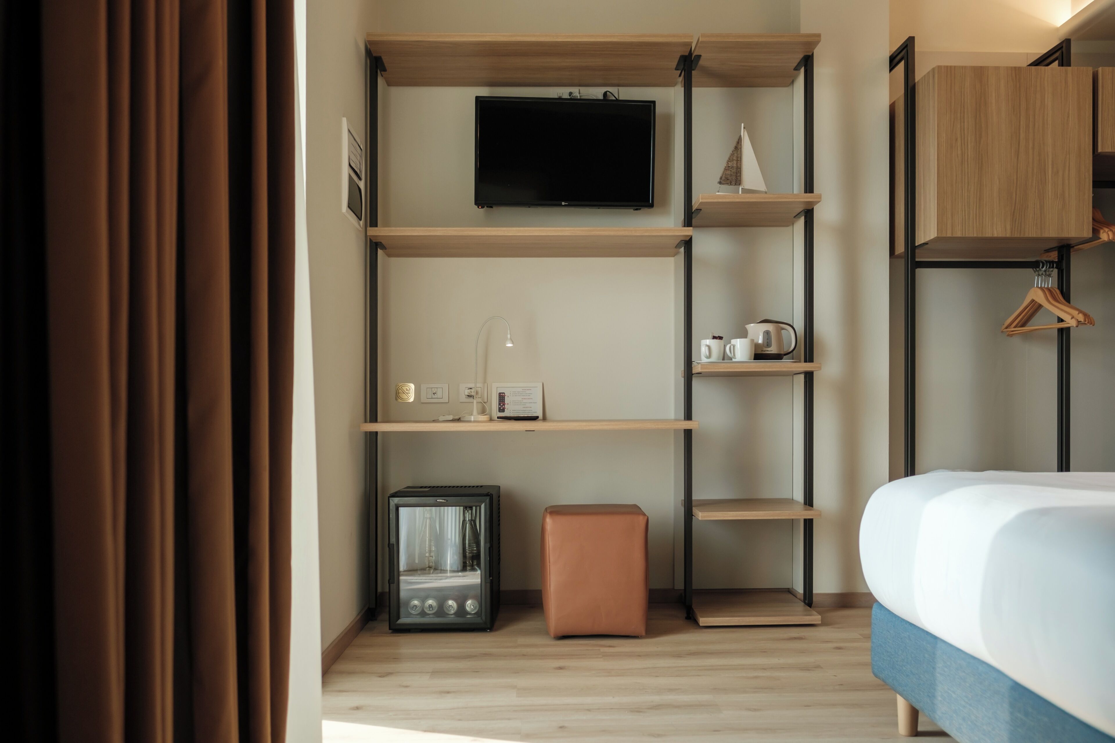 Ett modernt hotellrum med en säng, en TV som är monterad på väggen, ett litet bord med en lampa och en kaffemaskin.