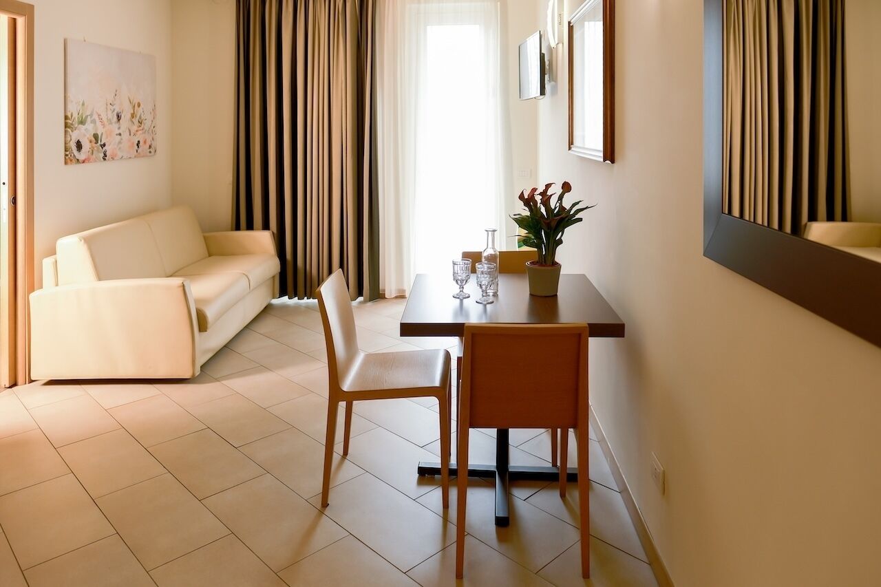 A room with a sofa, dining table, chairs, a potted plant, and a mirror.