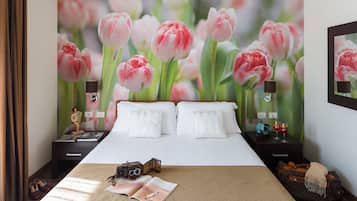 Une chambre d’hôtel avec un grand lit, deux tables de chevet, une valise, un appareil photo et un magazine posé sur le lit.