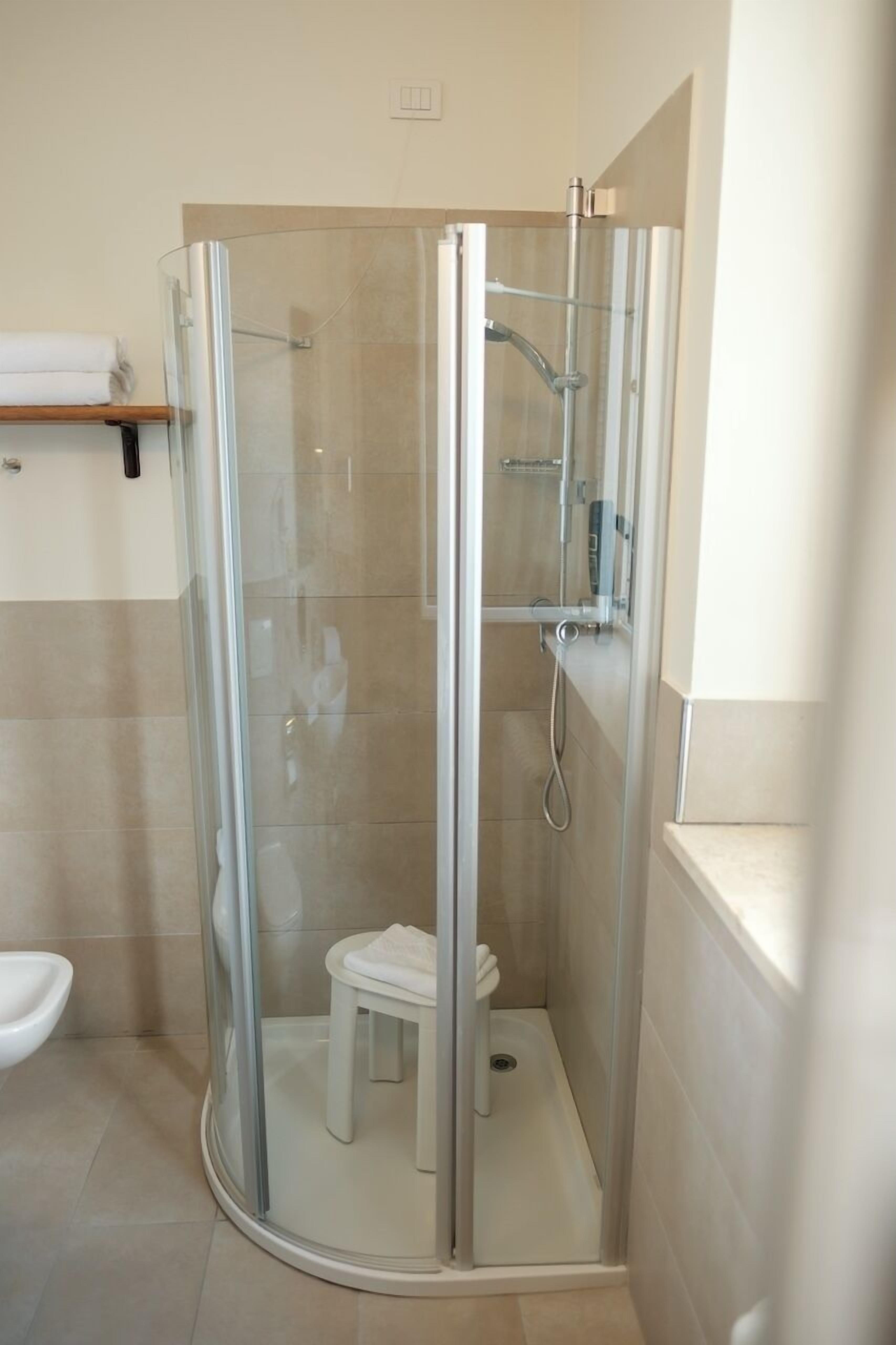 A modern bathroom with a glass-enclosed shower, a white toilet, and a small stool.