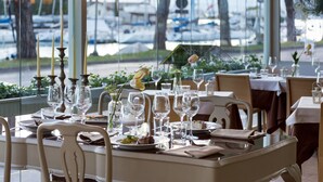 A dining area with tables set for a meal, chairs, and a view of boats through large windows. - Hotel Acquadolce (Peschiera del Garda)
