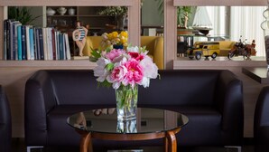 A modern living room with a glass coffee table, a black leather sofa, and a bookshelf filled with books and decorative items. - Hotel Acquadolce (Peschiera del Garda)