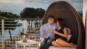 A couple sitting on a wicker chair overlooking a body of water, with a table between them holding a bottle of champagne and a glass. - Hotel Acquadolce (Peschiera del Garda)