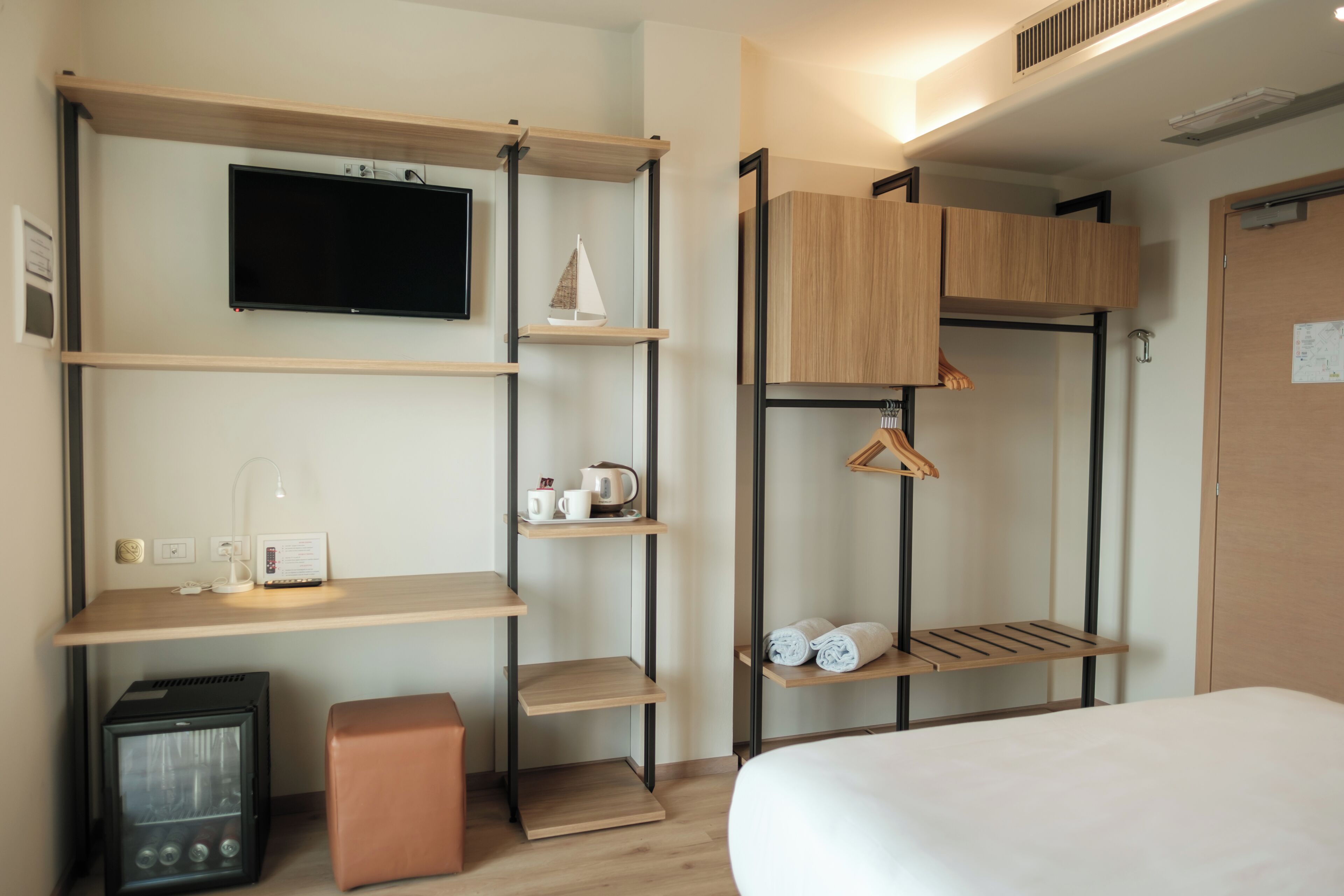 Une chambre d’hôtel compacte comprenant un lit, un téléviseur fixé au mur, une petite kitchenette et des étagères intégrées avec des espaces de rangement.
