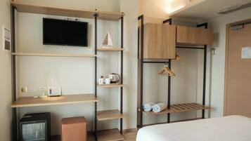 Une chambre d’hôtel compacte comprenant un lit, un téléviseur fixé au mur, une petite kitchenette et des étagères intégrées avec des espaces de rangement.