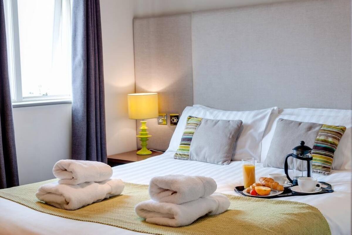 A hotel room with a bed, towels, breakfast tray, and a lamp.