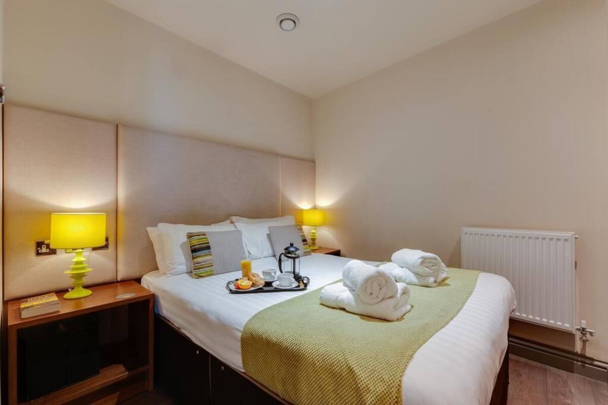 A hotel room with a bed, bedside lamps, a tray with breakfast items, and towels.